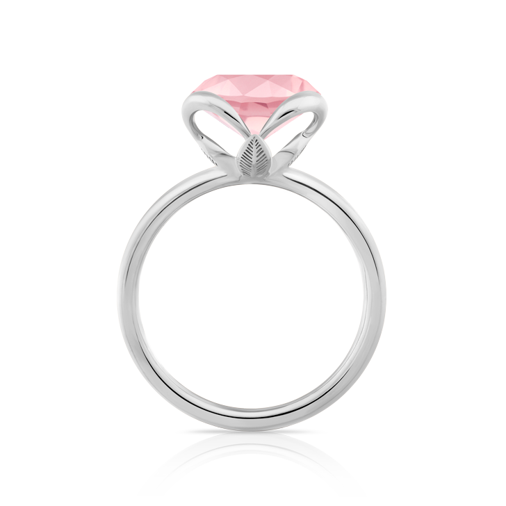 A Super White Gold 18K ring with a Pink Sapphire. The ring features an intricate design with a leaf motif beneath the gemstone setting. The Pink Sapphire is faceted and has a soft pink hue. The ring is shown from a side view, highlighting the detailed craftsmanship of the setting and the band.